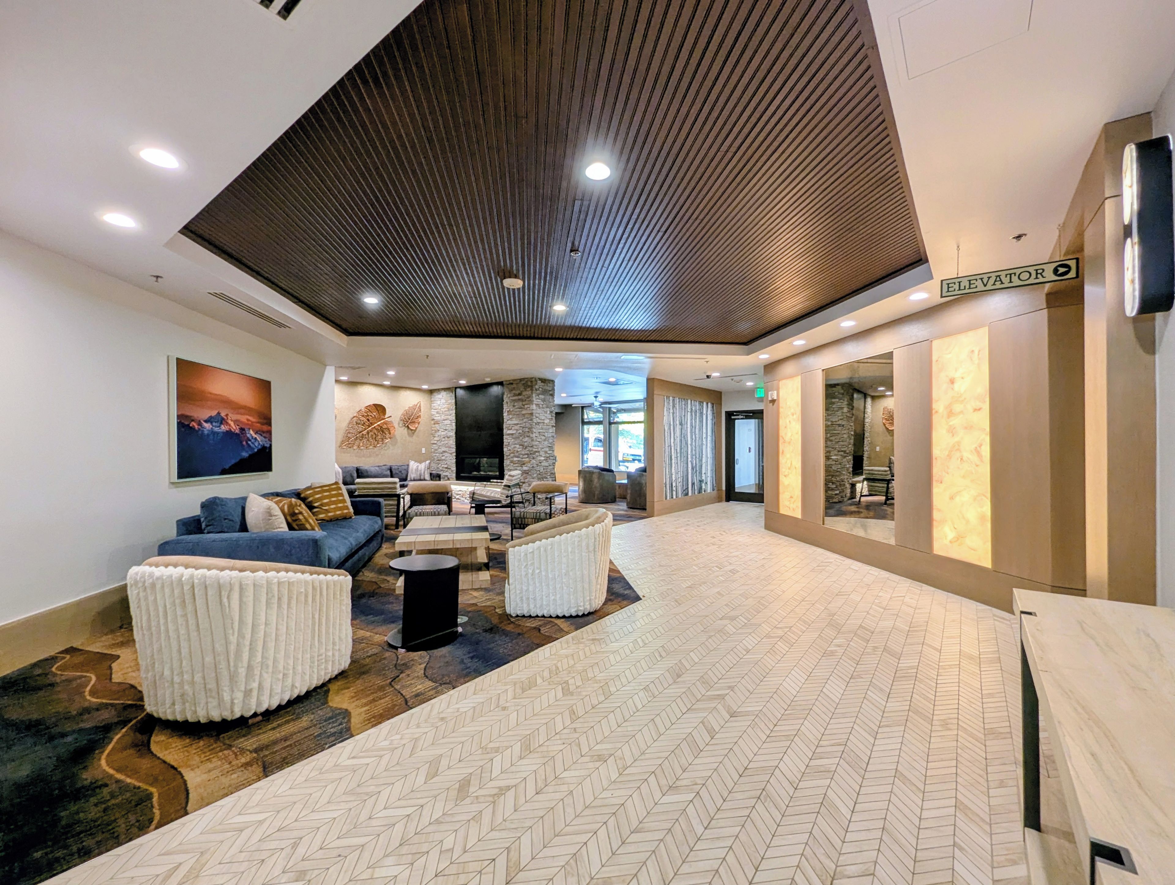 Een moderne lobby met een open haard, een zithoek en een bord met daarop een lift.