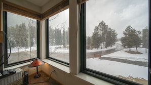 A room with a large window overlooking a snowy landscape, a lamp on a side table, and a basket on the floor. - Cozy Keystone Studio | Lake, Trails, + Pool (Keystone)