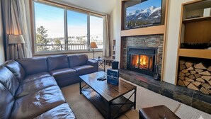 A living room with a leather sofa, a coffee table, a fireplace, and a TV mounted above it. - Cozy Condo w/Wood Fireplace & Indoor Pool/Hot Tubs (Keystone)