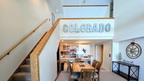 A spacious living area with a wooden staircase, a dining table with chairs, and a kitchen in the background. - Cozy Condo w/Wood Fireplace & Indoor Pool/Hot Tubs (Keystone)