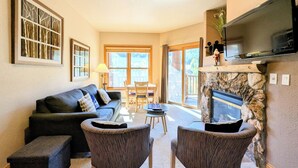 Un salon comprenant un canapé, deux fauteuils, une cheminée, un téléviseur et un coin repas avec une table et des chaises.