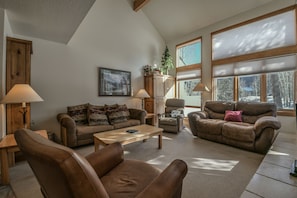 A spacious living room with a high ceiling, large windows, and a cozy fireplace.