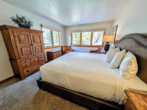 A bedroom with a large bed, wooden dresser, and a window with a view of trees. - Bright Updated 3B w/bunk room, Indoor Pool/Hot Tub (Keystone)