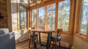 A dining area with a wooden table and chairs, large windows with a view of trees, and a stone wall. - Updated and Perfect for Families! (Keystone)