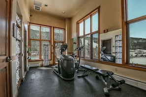 A gym with exercise equipment, large windows, and a view of a snowy landscape.