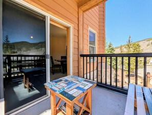 Une table en bois, dont le plateau est décoré d’une mosaïque, se trouve sur un balcon doté d’un mur en pierre et offrant une vue sur un paysage montagneux.