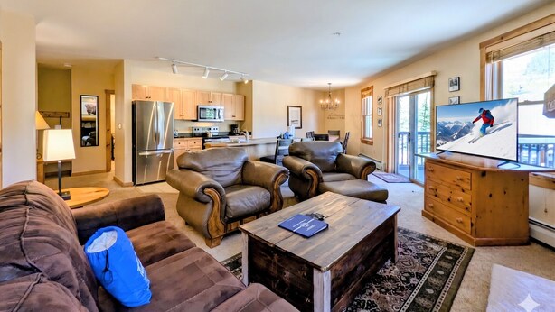 A modern living room with leather sofas, a wooden coffee table, a flat-screen TV, and a kitchen in the background. - Corner Unit | Hot Tub & Village Summer Fun (Keystone)