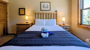 A bedroom with a wooden headboard, two bedside lamps, a framed picture above the bed, and a window on the right. - Corner Unit | Hot Tub & Village Summer Fun (Keystone)