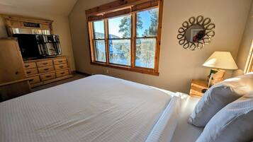 A bedroom with a large bed, wooden dresser, and a window with a view of trees.