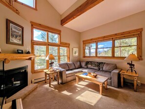 A cozy living room with a fireplace, large windows, a sofa, and a coffee table. - Tranquil Mountain Haven! Hot Tub and Shuttle (Keystone)