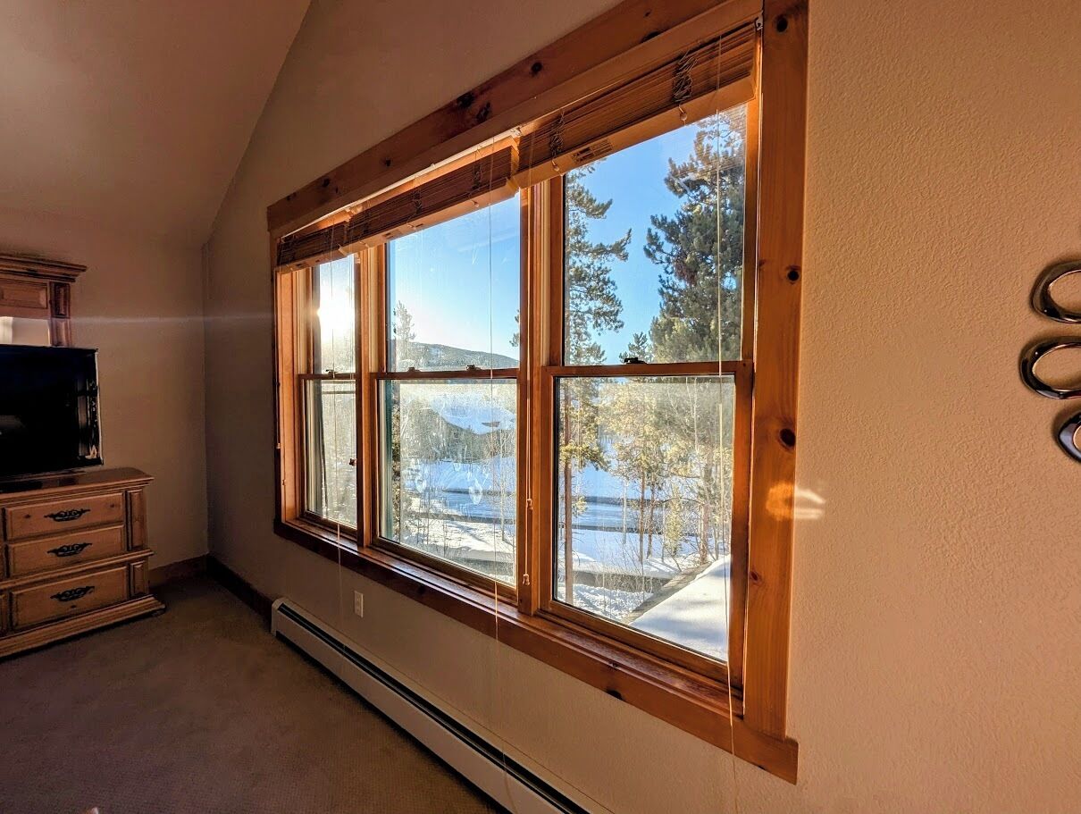 A room with a large window, a wooden dresser, and a thermostat.