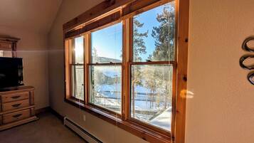 A room with a large window, a wooden dresser, and a thermostat.