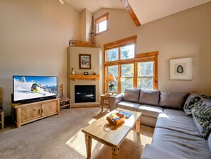 Settle into your sun-filled living room with soaring ceilings, warm wood accents, and a crackling fireplace. Large windows frame peaceful views of the surrounding landscape, while plush seating invites you to relax after a day of adventure.