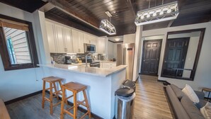 A modern kitchen with white cabinets, a stainless steel refrigerator, and wooden stools. - Modern Unit w/Pool & Hot Tub + 2 Parking Spots (Keystone)