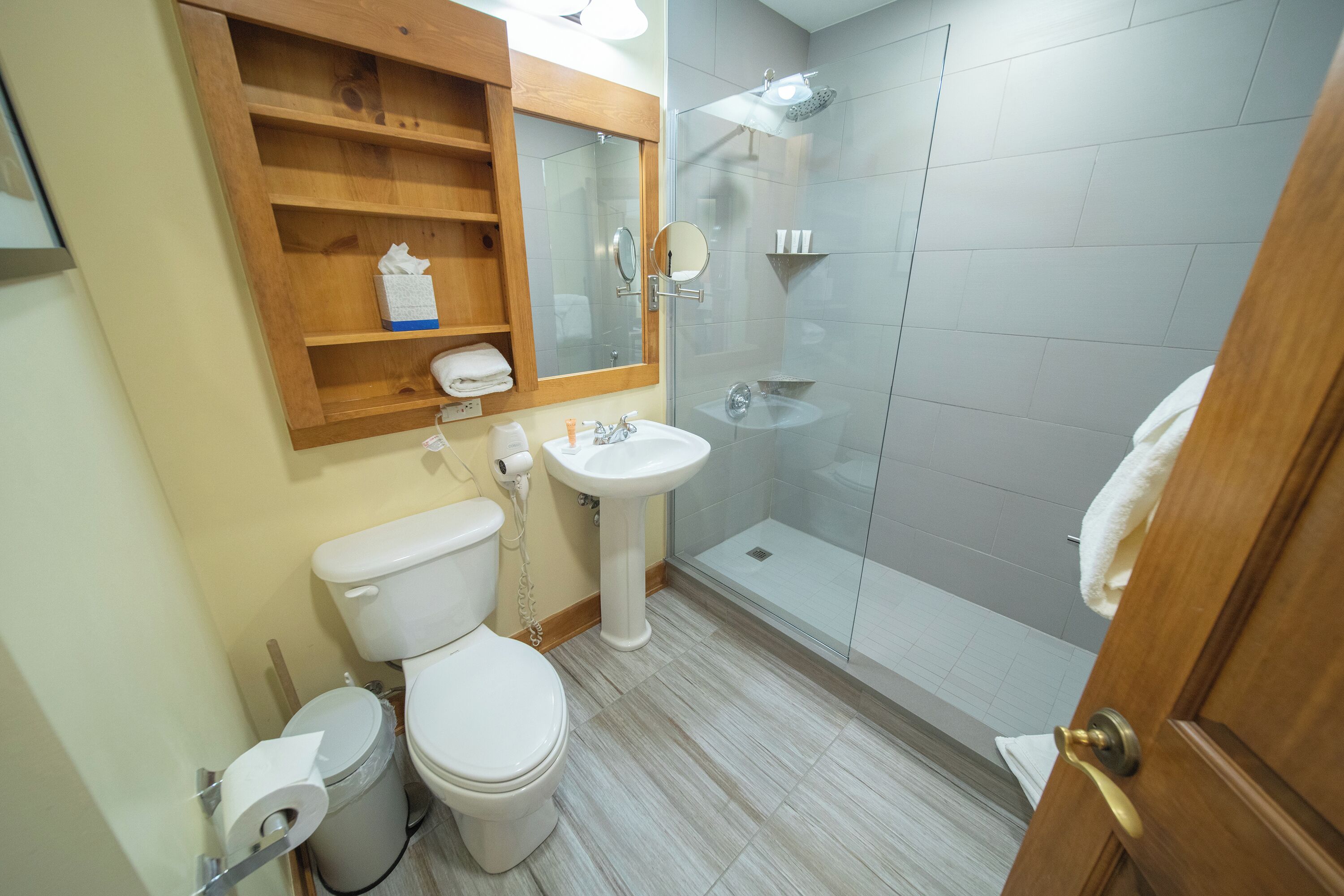 Et badeværelse med toilet, vask og brusebad med glasvæg.