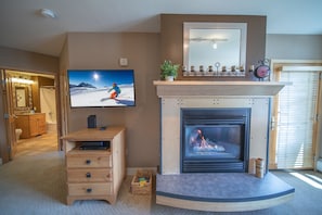 A living room with a fireplace, a television mounted on the wall, and a wooden cabinet.