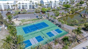Ein Küstenhotel mit mehreren weißen Gebäuden, einem Tennisplatz und Blick auf den Strand.