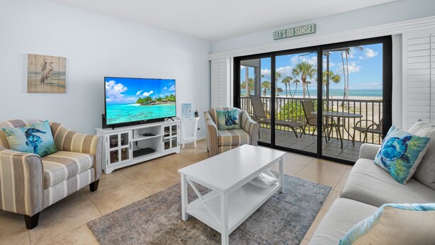 Ein Wohnzimmer mit Fernseher, Sofas, einem Couchtisch und Blick auf den Strand durch große Schiebetüren.