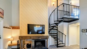 A living room with a fireplace, a TV mounted on the wall, and a spiral staircase. - Quiet, Outdoor Pool/Indoor Hot Tub, Shuttle (Keystone)