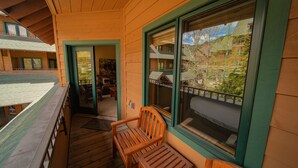A wooden deck with a wooden bench and a large window offering a view of a building with multiple windows and balconies.
