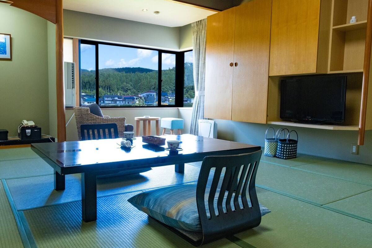 Una habitación con una mesa de comedor, sillas, televisión y vistas a un área boscosa.
