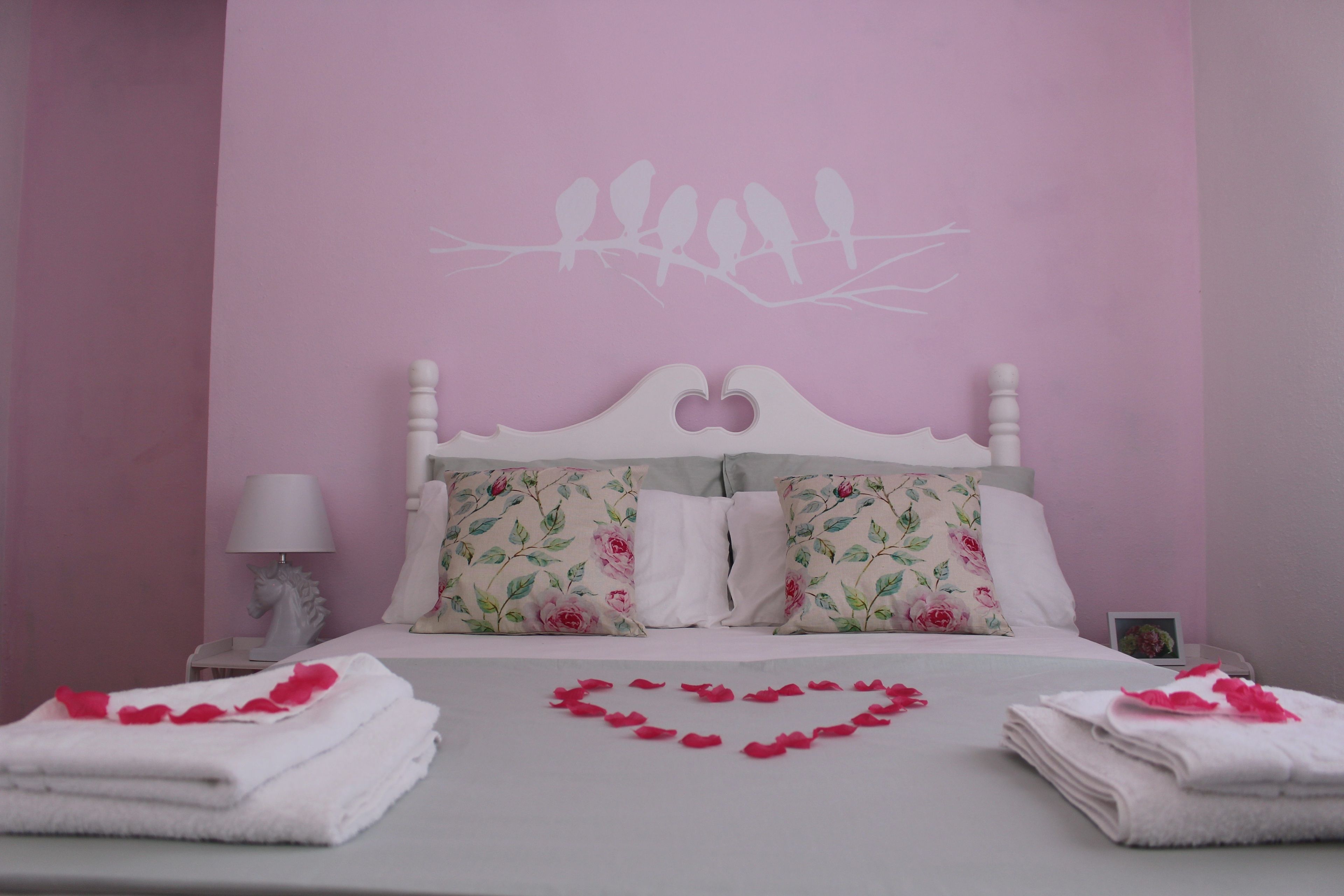 A bedroom with a bed, pillows, a nightstand, a lamp, and a heart-shaped decoration on the bed.
