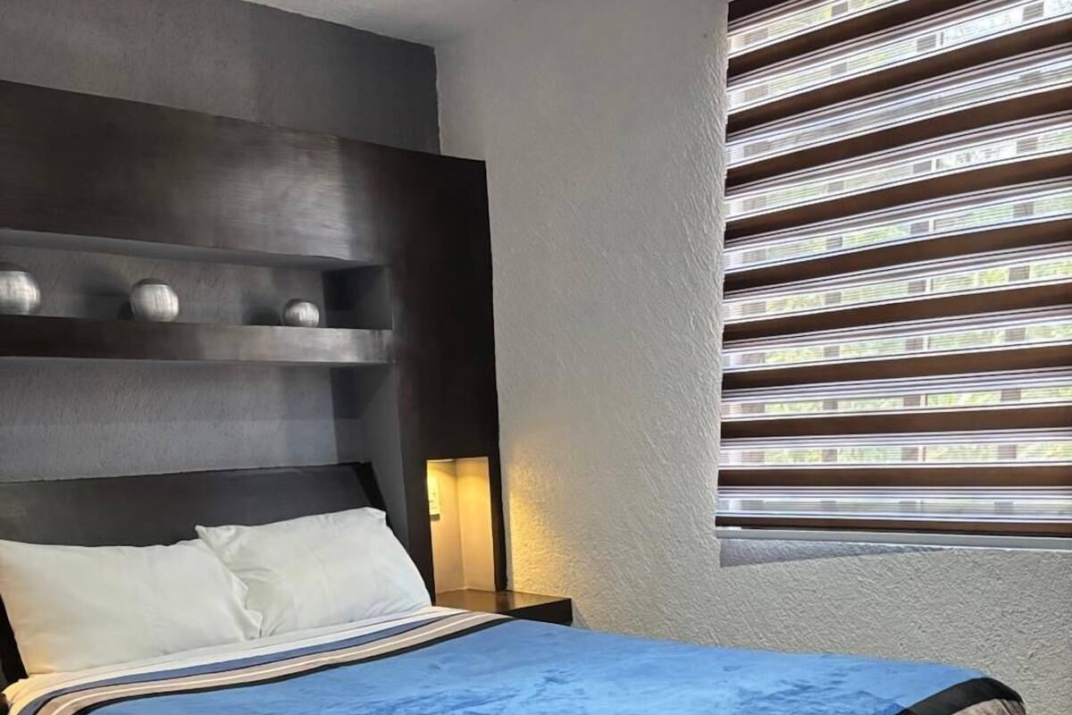 A neatly made bed with a blue cover, a dark headboard, and a nightstand with a lamp.