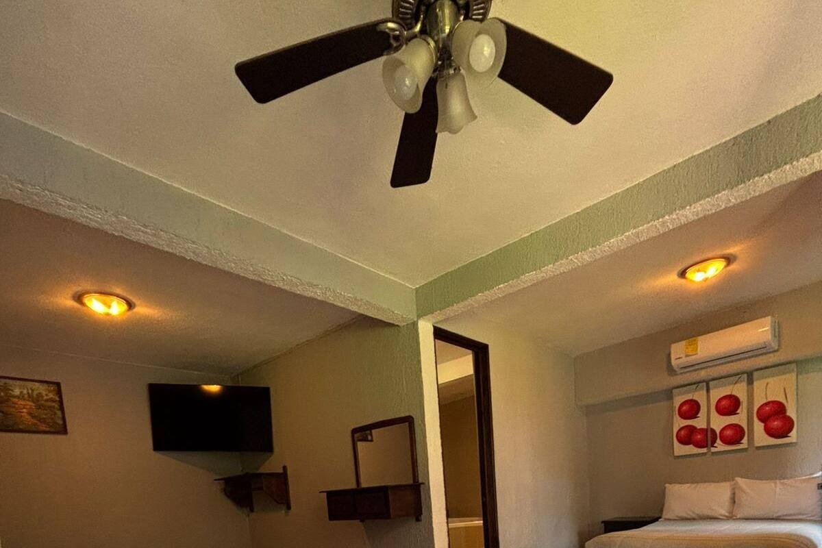A bedroom with two beds, a ceiling fan, a TV, and a wall-mounted air conditioner.