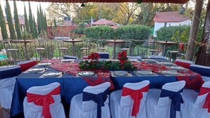 An outdoor dining area with tables set for a meal, chairs with red and white sashes, and a garden view in the background. - Hotel Real Campestre Tepetoci (Tepeji del Río de Ocampo)