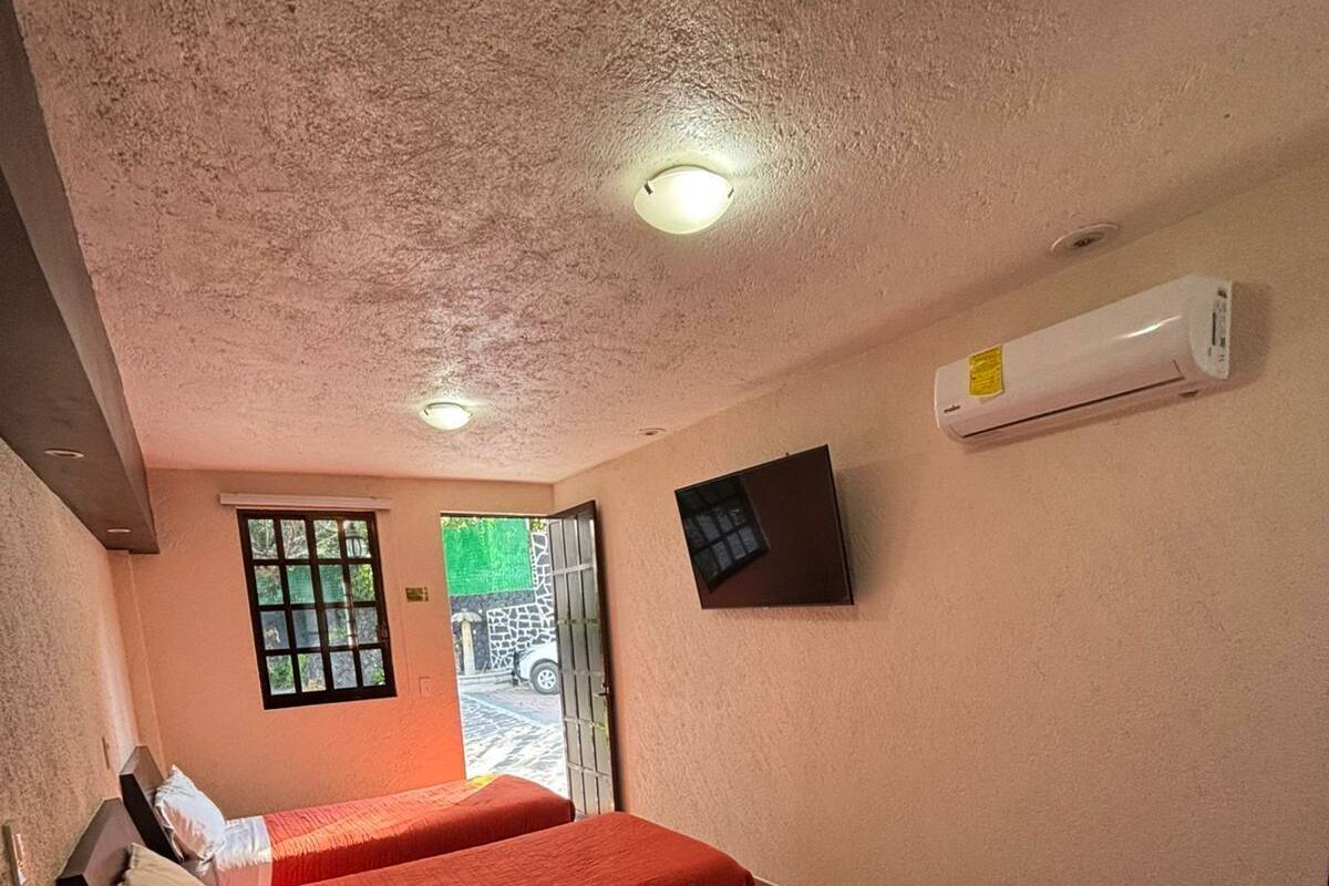 A hotel room with two beds, a window, an air conditioning unit, and a door leading outside.
