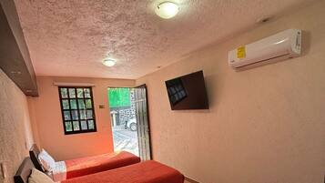 Una camera d'albergo con due letti, una finestra, un condizionatore e una porta che dà sull'esterno.