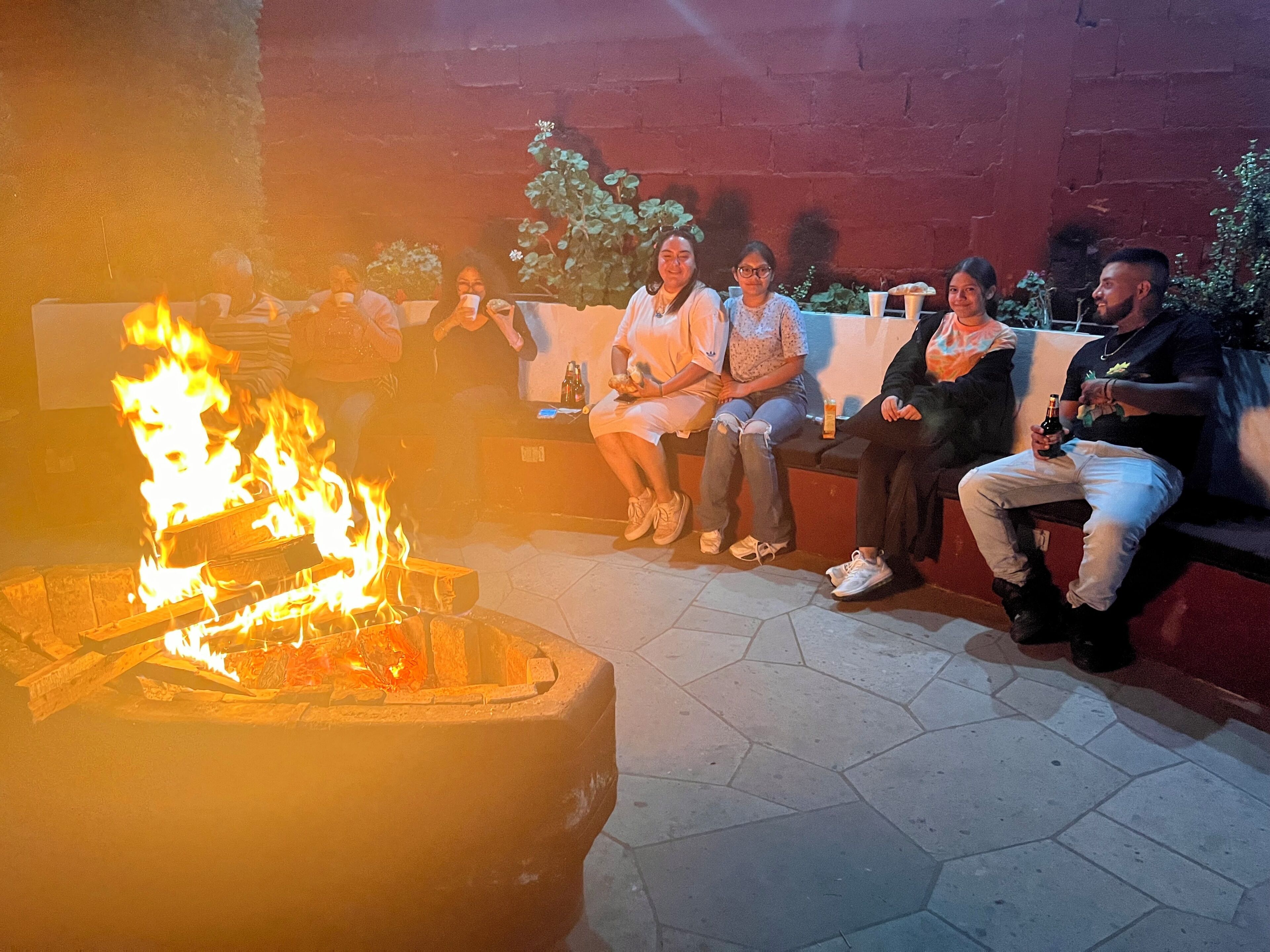 A group of people seated around a fire pit in an outdoor setting.