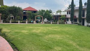 A courtyard with a lawn, a gazebo, and buildings with a red roof and a green awning. - Hotel Real Campestre Tepetoci (Tepeji del Río de Ocampo)