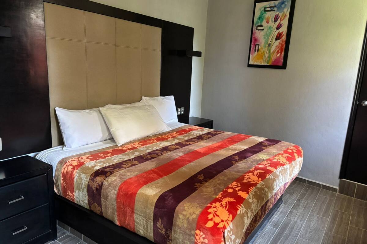A neatly made bed with a striped bedspread, a dark headboard, and a small bedside table with drawers.
