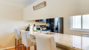 A modern kitchen with a granite countertop, stainless steel appliances, and a bar seating area. - Walk to Bethany Beach Boardwalk: Coastal Retreat (Bethany Beach)