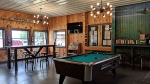 A pool table in a room with wooden walls, a sign reading "NORTH TWIN LODGE", and a bar area with books. - Amenities & Resort Access Included, Cabin 13 (Phelps)