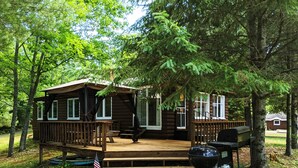 A rustic cabin with a deck, surrounded by trees. - Amenities & Resort Access Included, Cabin 13 (Phelps)
