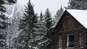 A log cabin with a stone foundation, surrounded by snow-covered trees. - Amenities & Resort Access Included, Cabin 13 (Phelps)