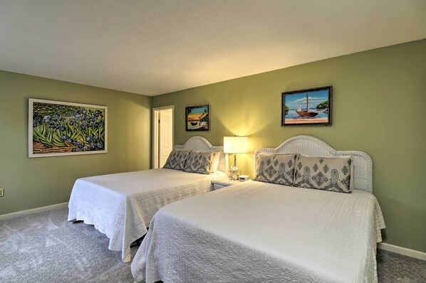 A room with two beds, a nightstand with a lamp, and two paintings on the walls.
