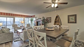 A dining area with a wooden table and white chairs, a ceiling fan, and a view of the outdoors through large windows. - 4 Mi to Lake: Unit w/ Pool Access in Fairfield Bay (Fairfield Bay)