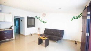 A spacious living area with a dark sofa, a small coffee table, and a kitchen area with cabinets and a countertop. - DEPARTMENT FOR 5 PEOPLE. EXCELLENT LOCATION (Playa del Carmen)