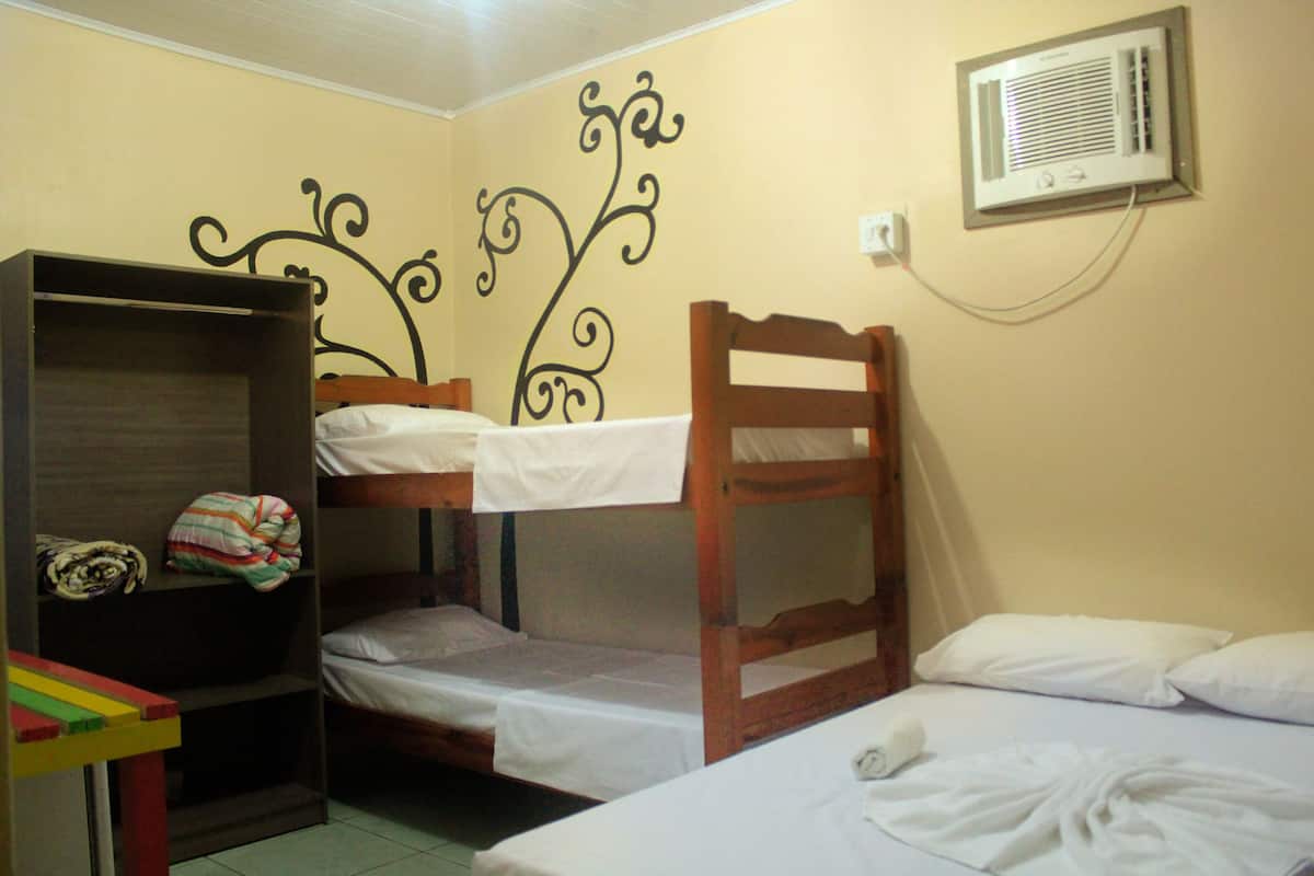 A bunk bed room with a wooden headboard, a shelf with folded clothes, and a wall-mounted air conditioner.
