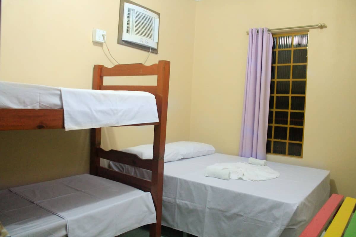 A room with bunk beds and a single bed, a window with a curtain, and a wall-mounted air conditioning unit.