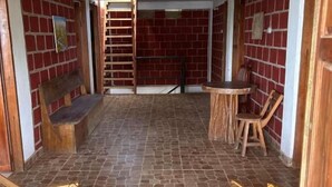 Une pièce avec un mur en briques, une échelle en bois, une chaise en bois, une petite table et un banc.