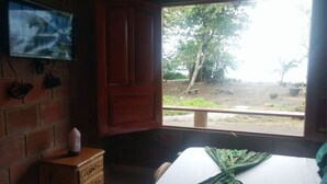 Una habitació amb un llit, un televisor fixat a una paret de maó i una finestra amb vista a arbres i un camí de terra.