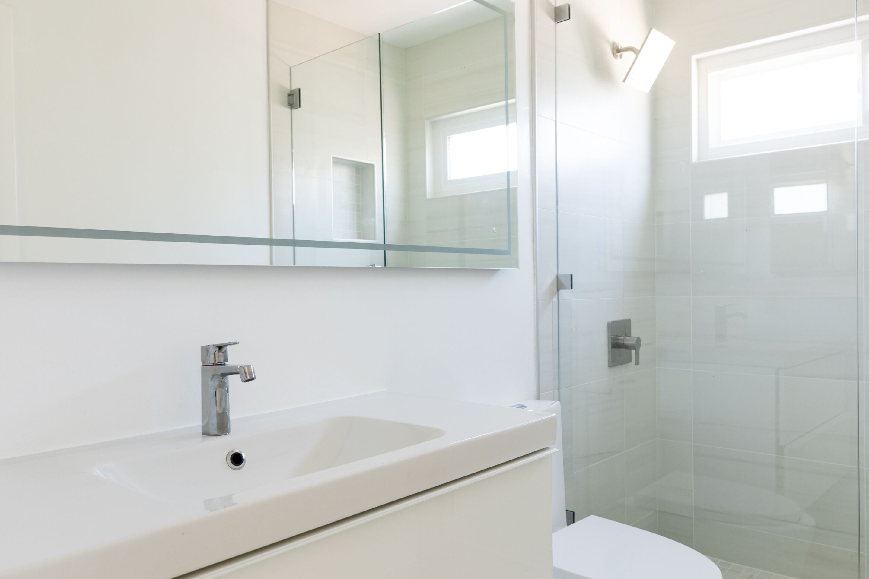 Un baño moderno con cabina de ducha de vidrio, un lavabo blanco y un espejo grande.