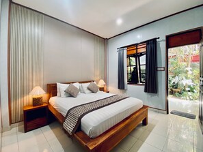 Un dormitorio moderno con una cama de madera, dos mesitas de noche con lámparas, vistas a zonas verdes a través de una ventana y una puerta corredera que da al exterior.