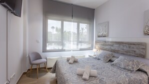 Un dormitorio con una cama grande, una silla, un televisor y una ventana con vistas a palmeras.