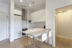 A modern kitchen with white cabinets, a stainless steel refrigerator, a microwave, and a sink. There are four white bar stools around the kitchen island. - ApartUP Patacona Beach Select (Alboraya)
