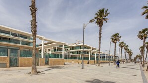 Un edificio moderno con fachada de vidrio, una galería techada y palmeras a lo largo de la calle.